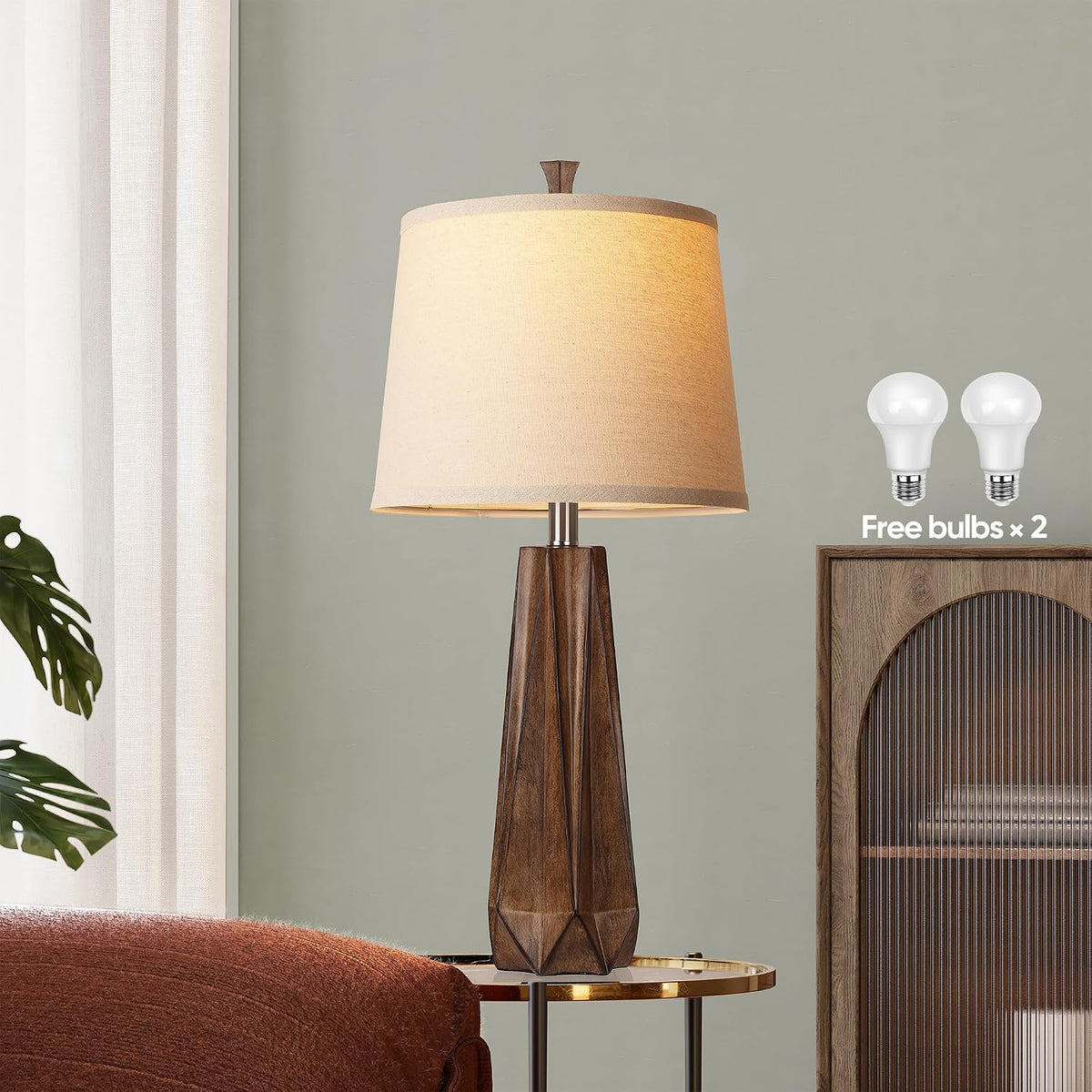 Wood-grain table lamp on side table with two LED bulbs pictured and beige linen shade