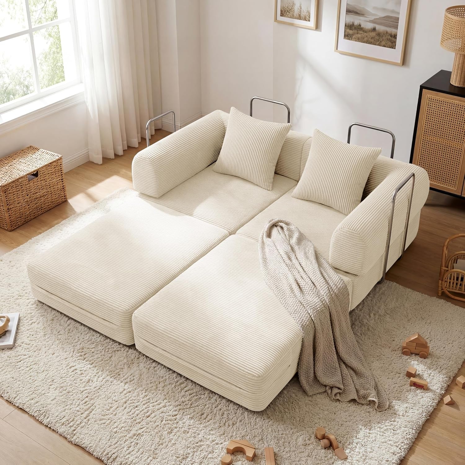 Cream corduroy folding sofa converted flat into a low double-bed with pillows, throw and scattered wooden toys.