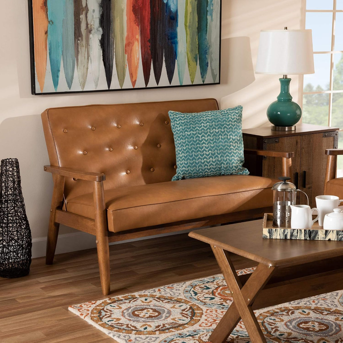 Tan faux leather loveseat in a living room setting with patterned rug, side table and a blue accent pillow