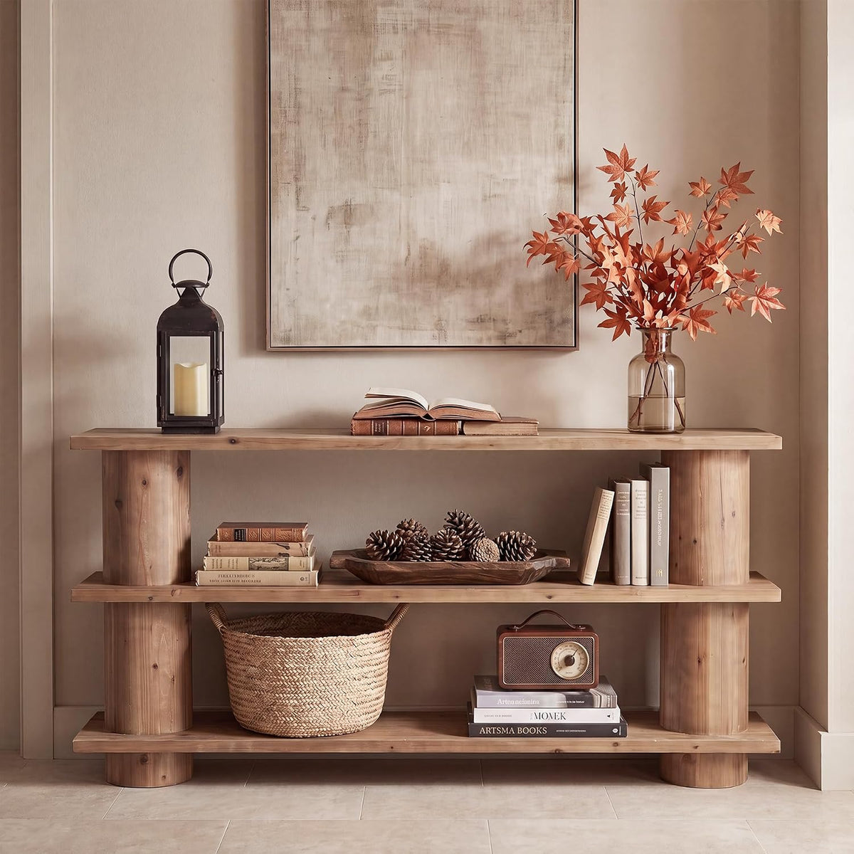 Three-tier solid wood console table in a natural finish styled with a lantern, open book and vase, front view