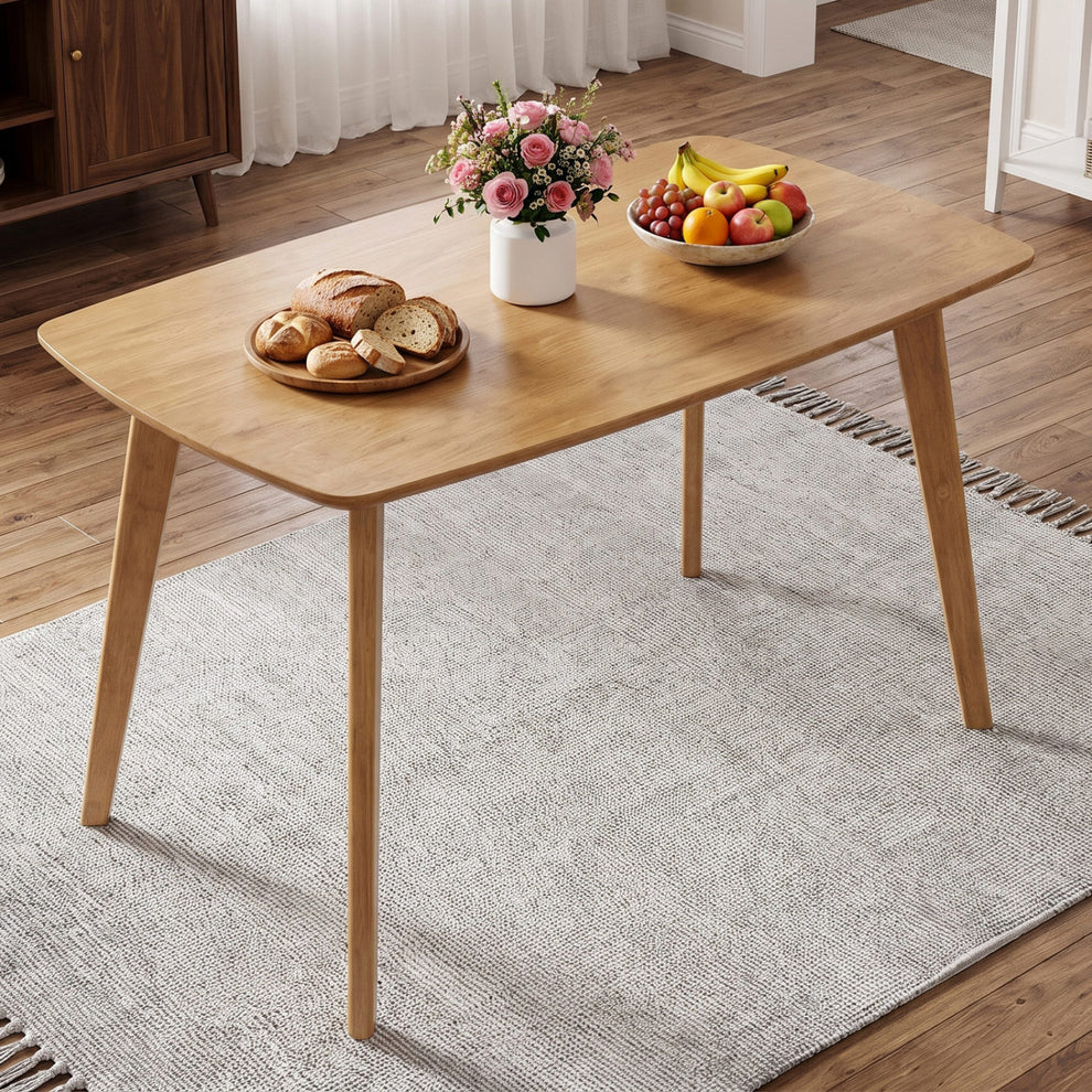 Natural wood dining table with rounded corners, styled with flowers and fruit on a rug