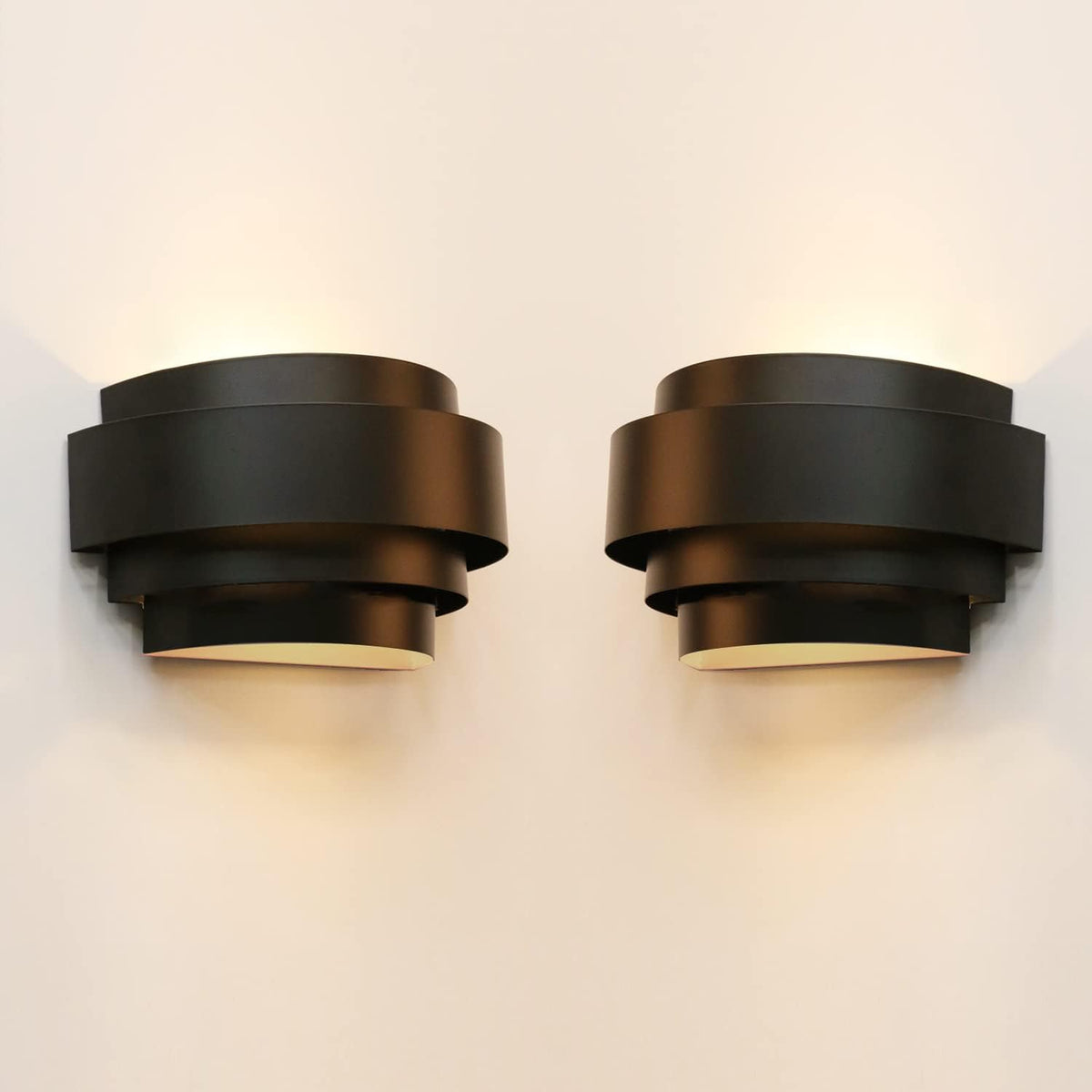 Two black stepped half‑moon wall lights mounted side by side, glowing softly against a pale wall.