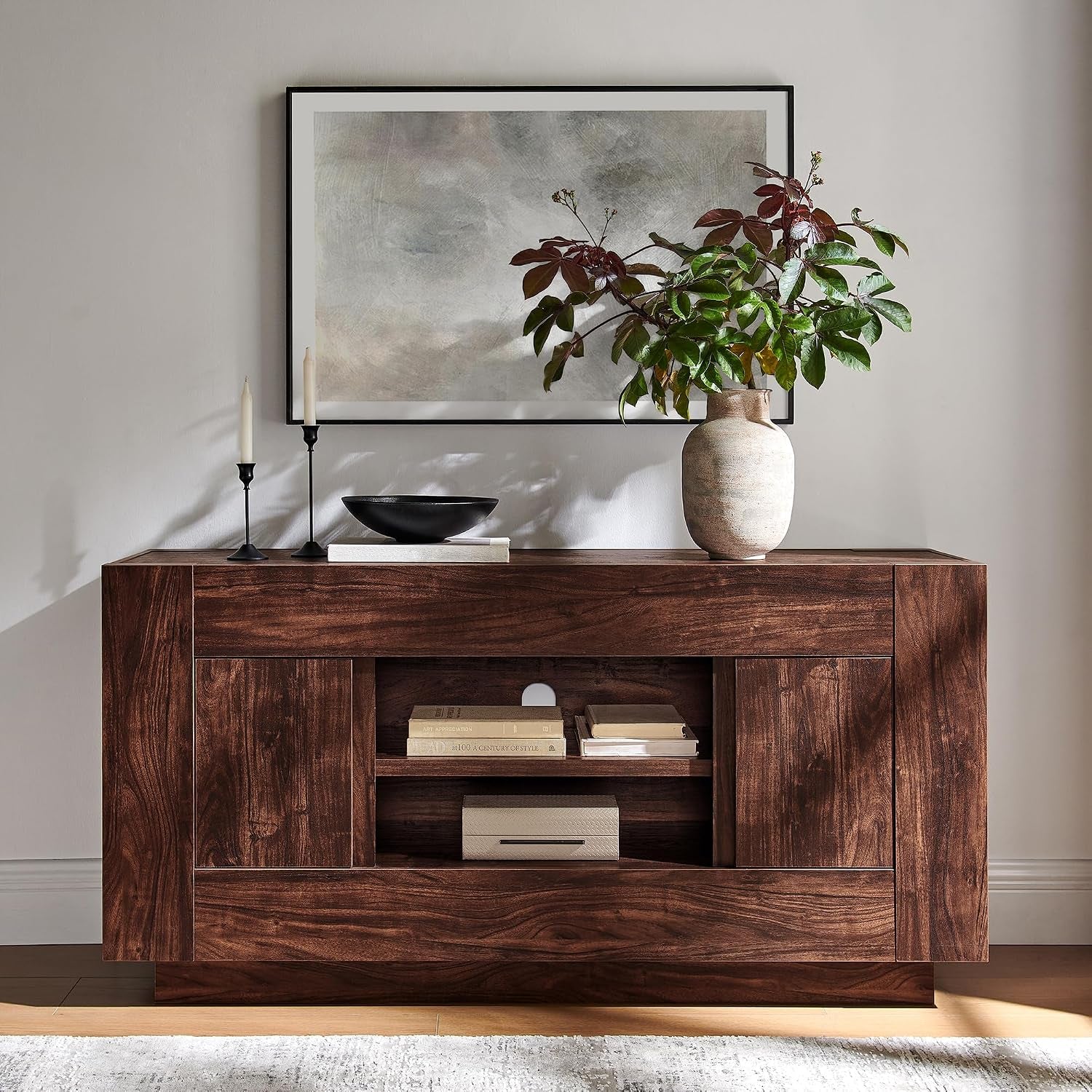 Medium walnut console table with central cubby shelves, vase and candles on top, framed art above