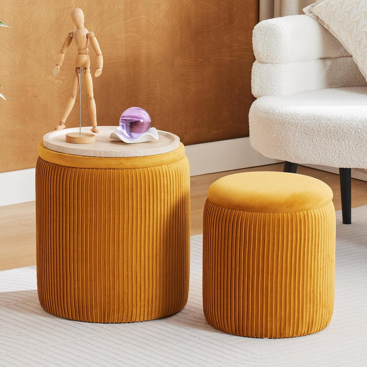 Mustard yellow ribbed velvet ottoman set, larger with wood top and smaller with smooth padded lid near a cream chair.