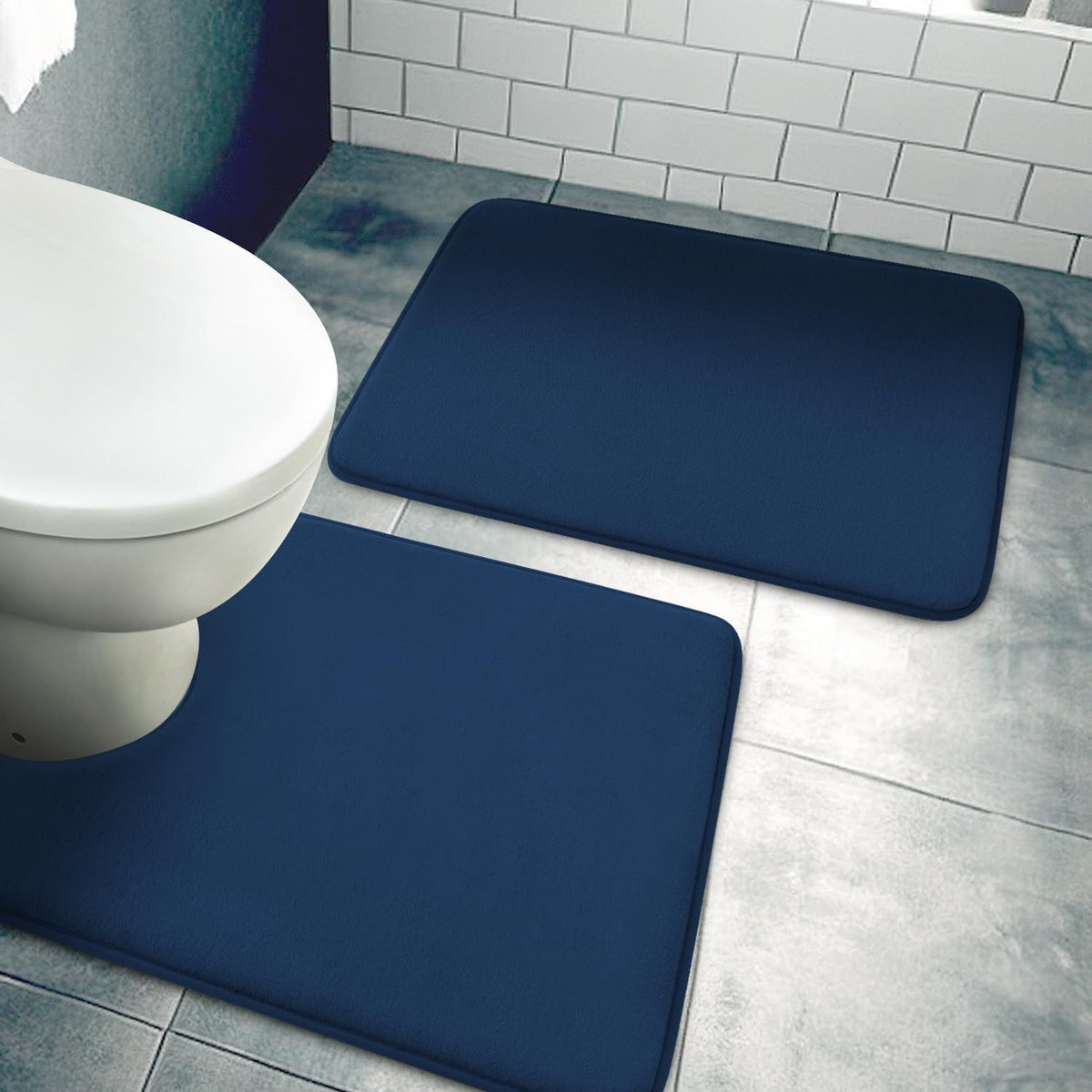 Overhead view of navy blue rectangular bath mats positioned around a toilet on mottled tile flooring.