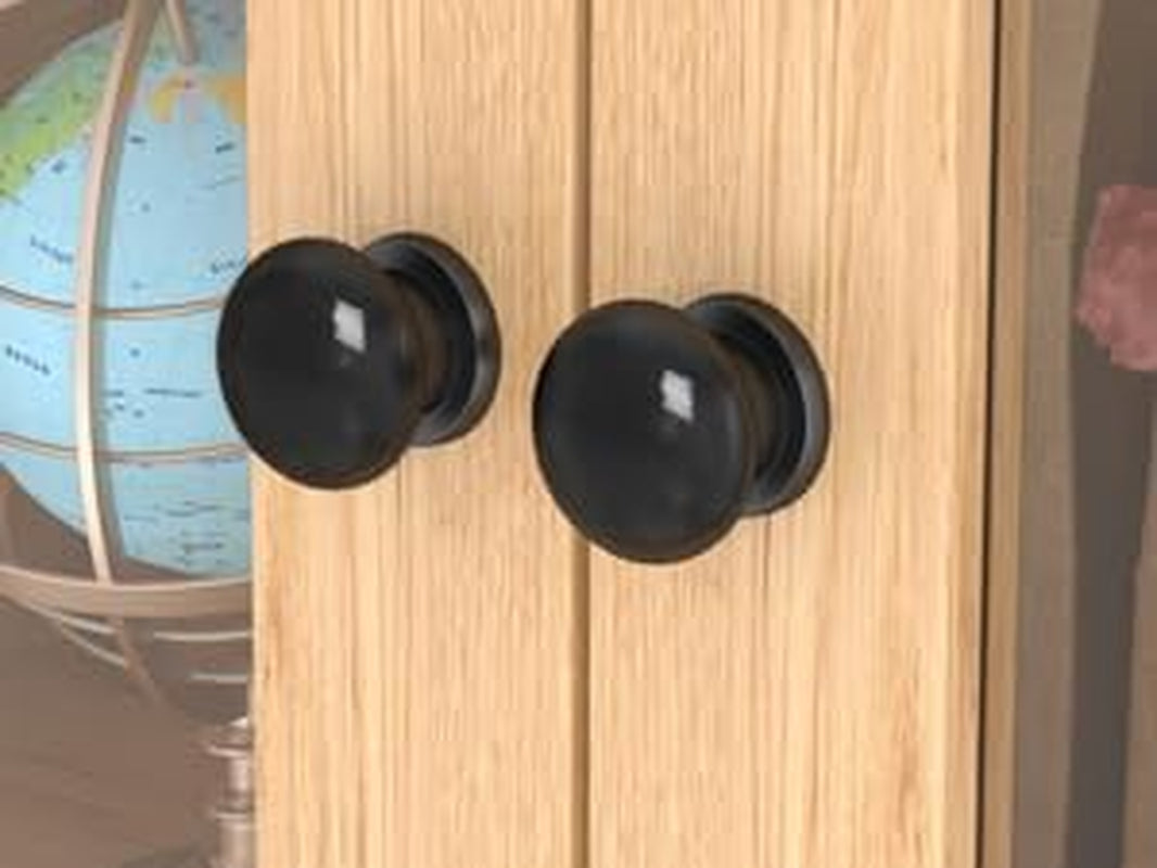 Close-up of two round matte black drawer knobs mounted on light wood cabinet doors.