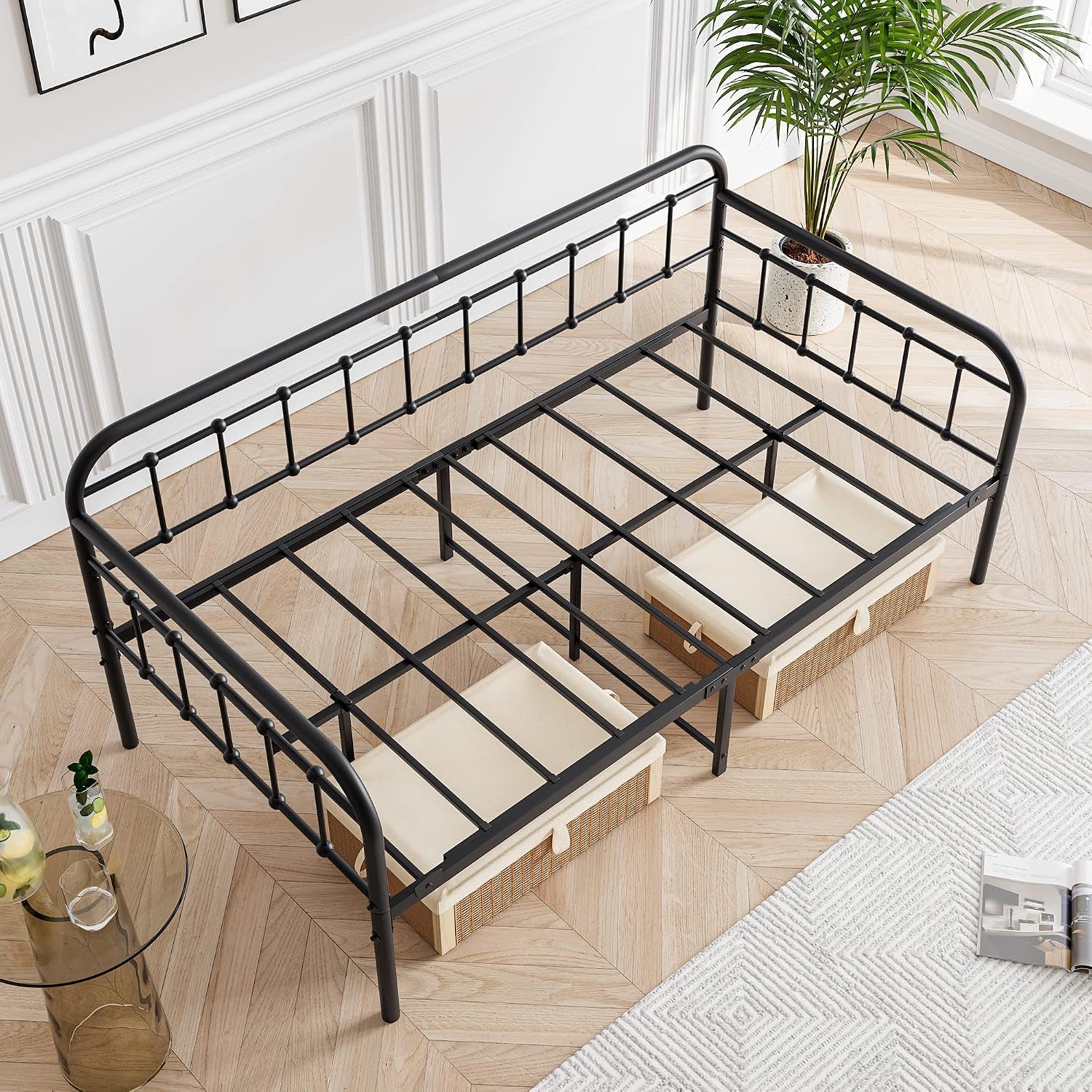 Aerial angle of the black metal daybed showing slat layout and two storage baskets tucked under the frame