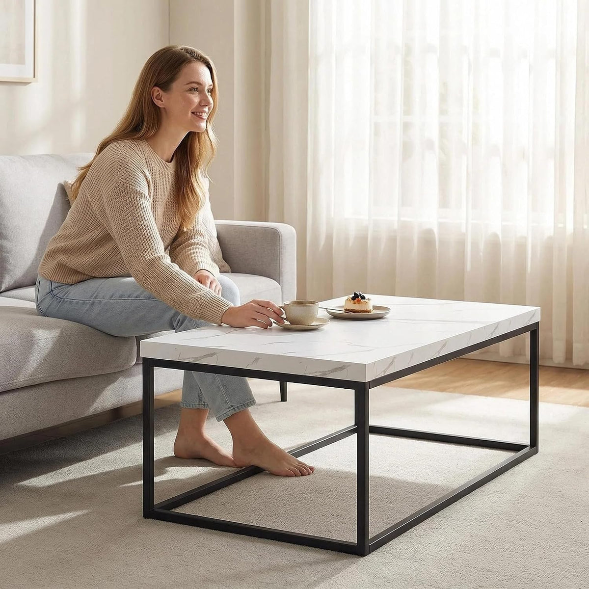 Person seated on a sofa reaching toward a white marble tabletop coffee table in a lifestyle scene