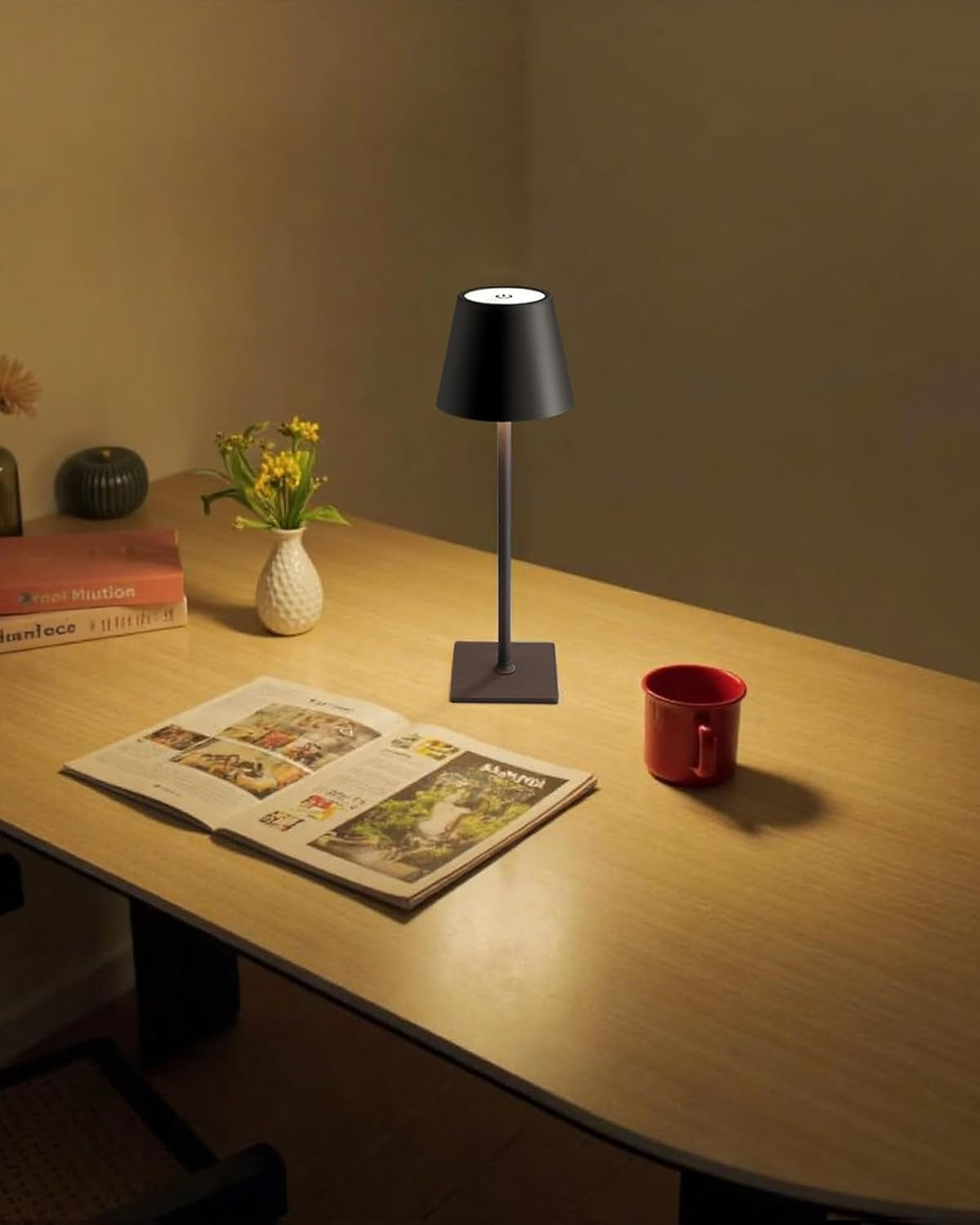 Single black lamp on a wooden desk illuminating an open magazine and a red mug in a cozy reading setup.