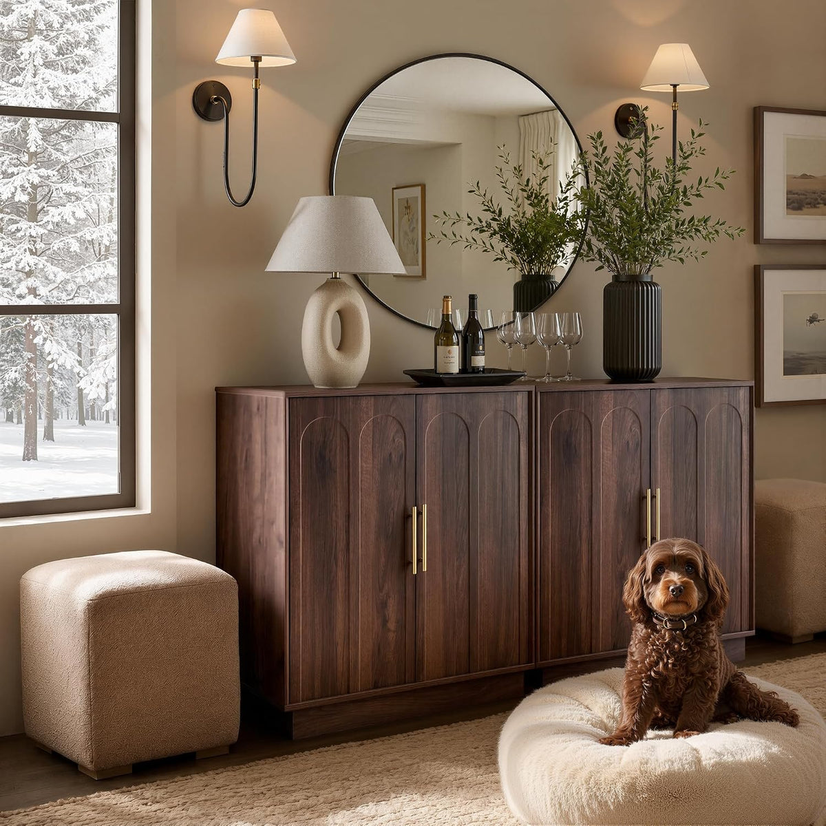 Wide shot of two walnut cabinets under a round mirror with wall sconces; a small brown dog sits on a plush pouf in front.