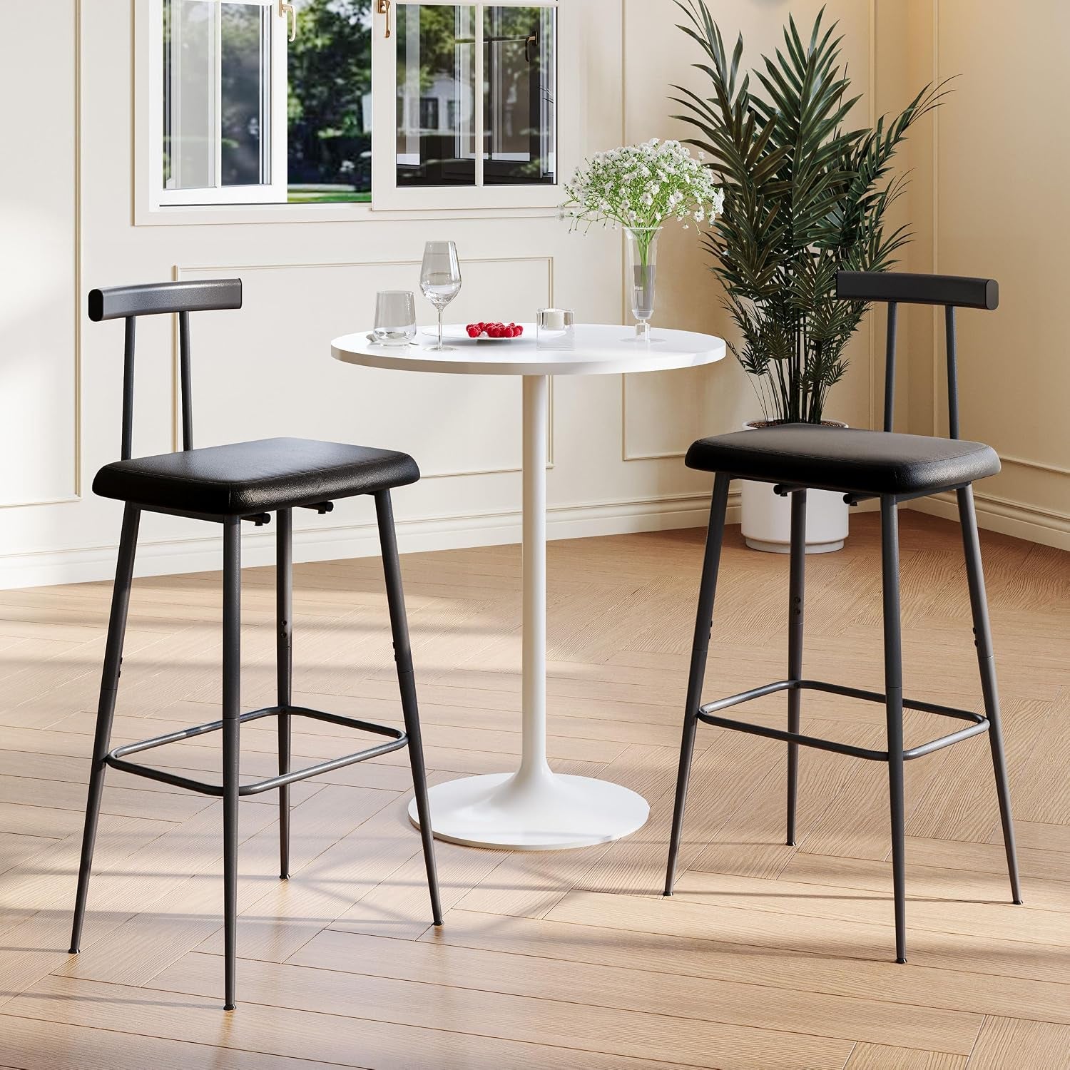 Two black counter stools flanking a small white round table in a bright, neutral dining room setting