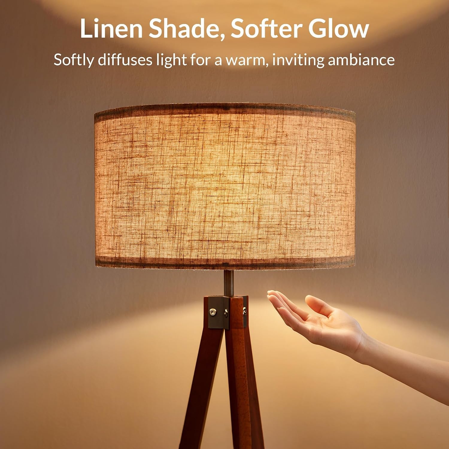Lit beige linen drum shade on tripod lamp showing the soft diffused glow with a hand nearby