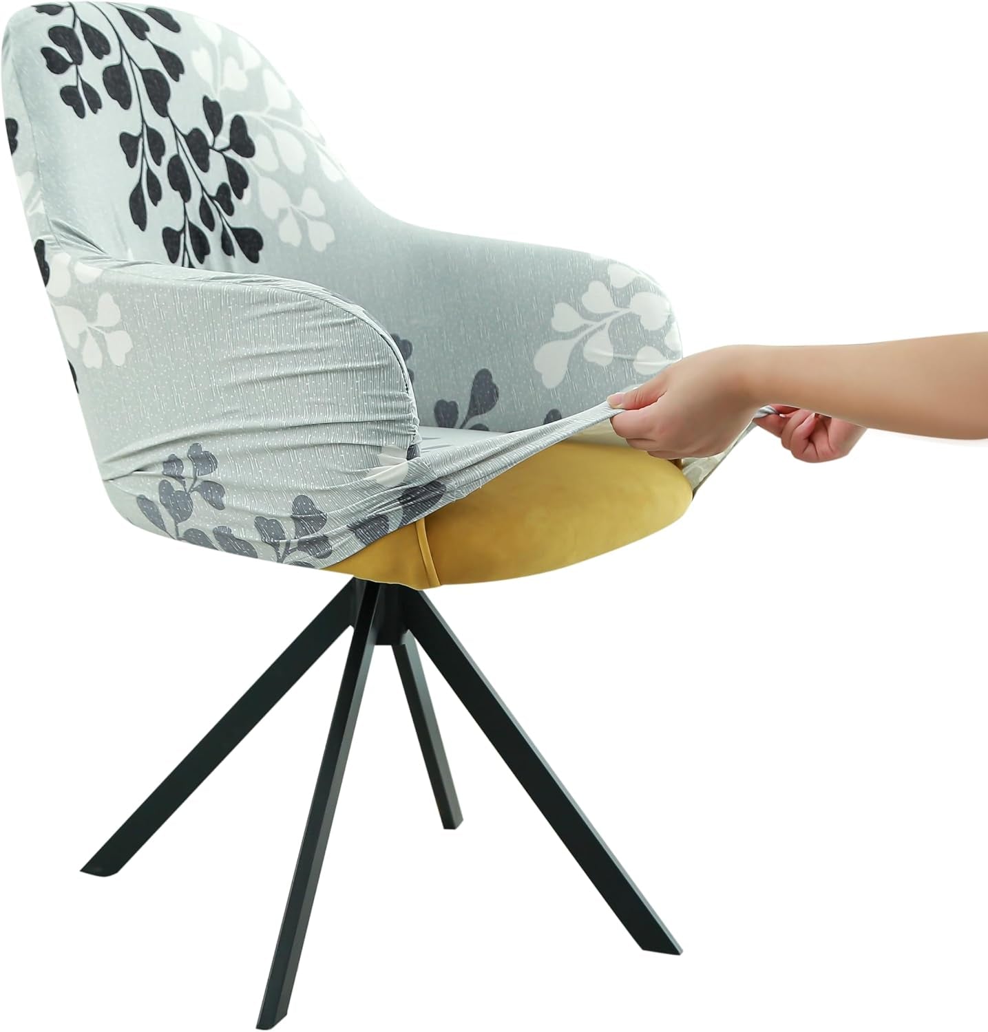 Side view of a light gray cover with dark leaf motifs being pulled down over a chair seat by two hands.