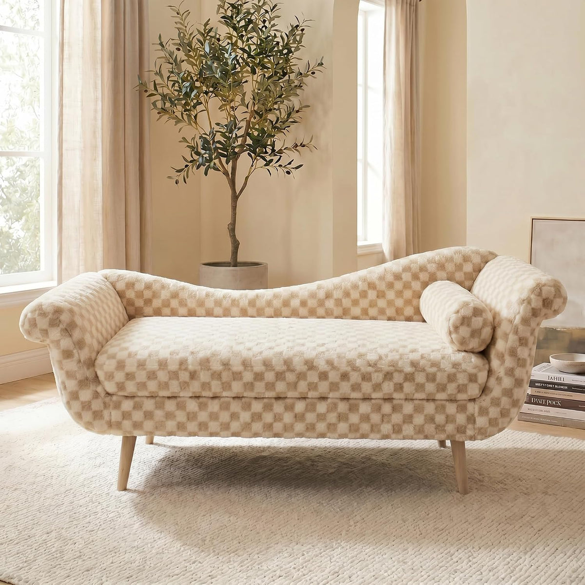 Cream checkered chaise lounge front view in a warm room with a potted plant and stacked books on the floor