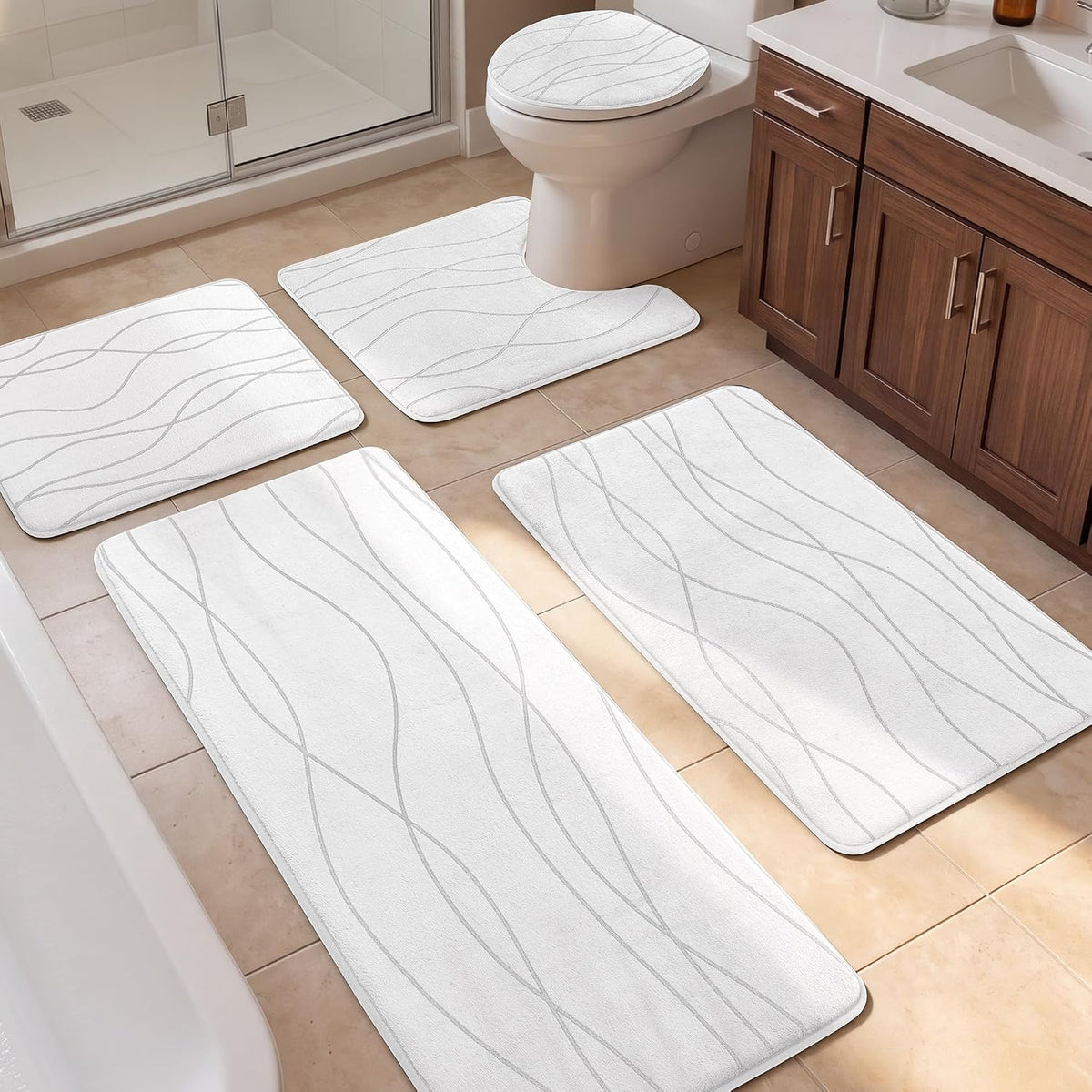 Five white patterned bath rugs arranged around a toilet, tub and vanity on tan tile floor.