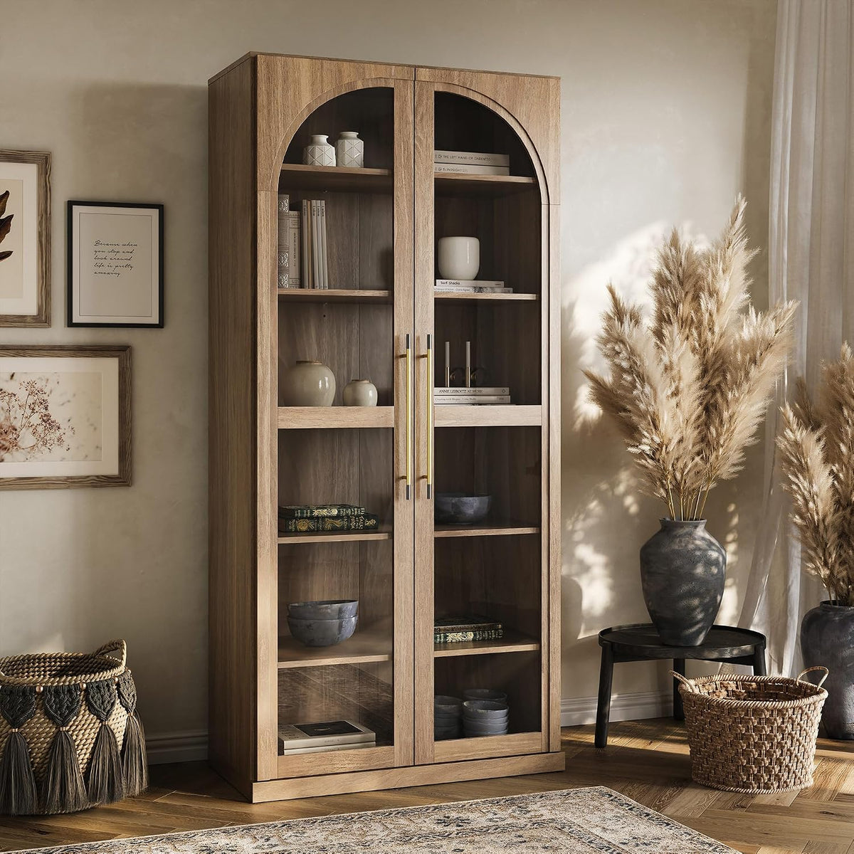 Tall glass-front curio cabinet in a light wood finish staged in a living room with decor