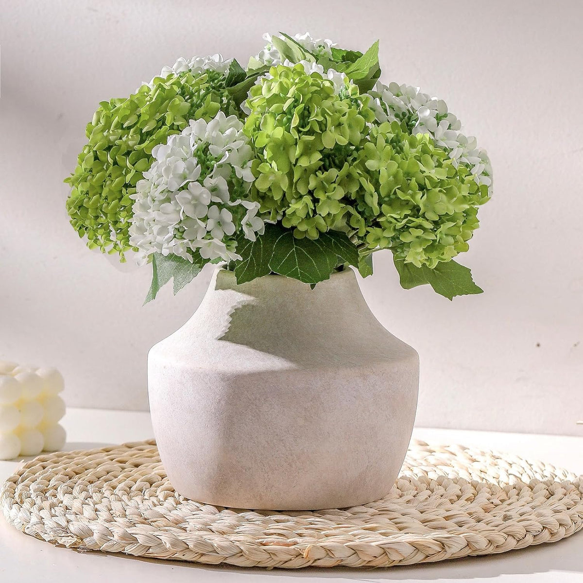 Close-up of a low rounded vase neck with clustered green-and-white blossoms and soft textured shadows.