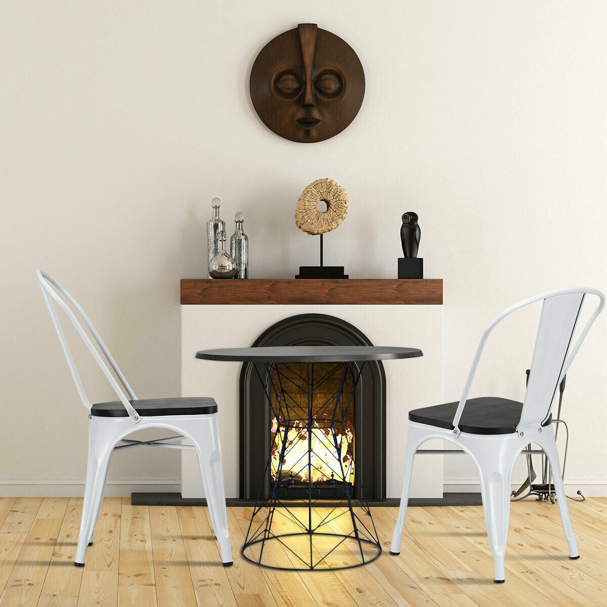 Two white metal chairs with dark seats flank a small round table in front of a fireplace.