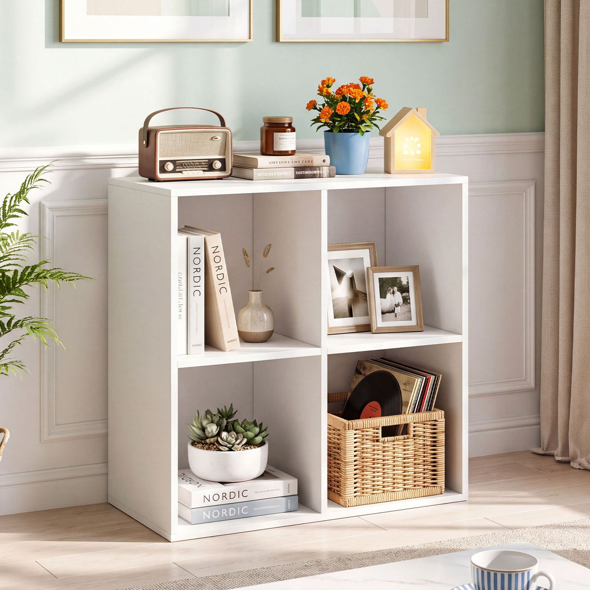White four-cube bookshelf styled with books, framed photos, a plant and a woven basket.