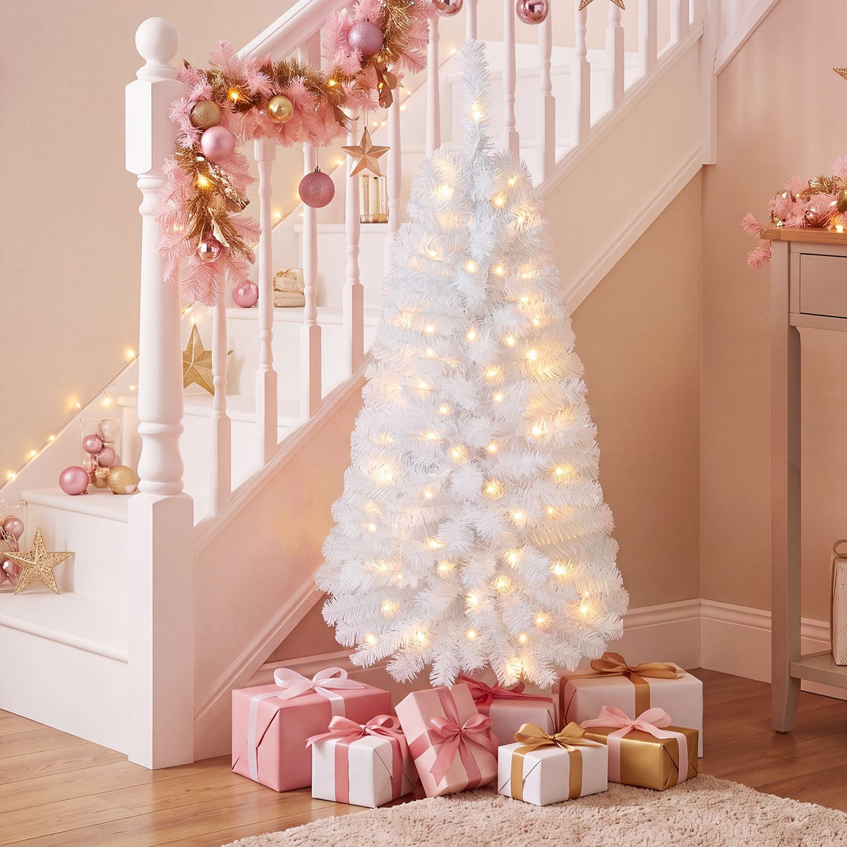 A glowing white Christmas tree with pink and gold decorations stands beneath a staircase, surrounded by gifts.