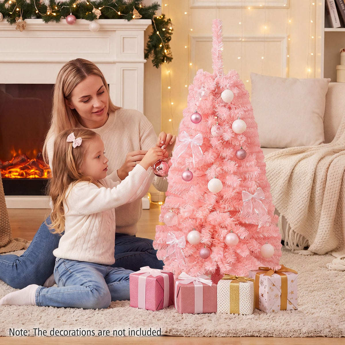 A woman and child decorate a pink Christmas tree beside a fireplace, with wrapped gifts at its base.