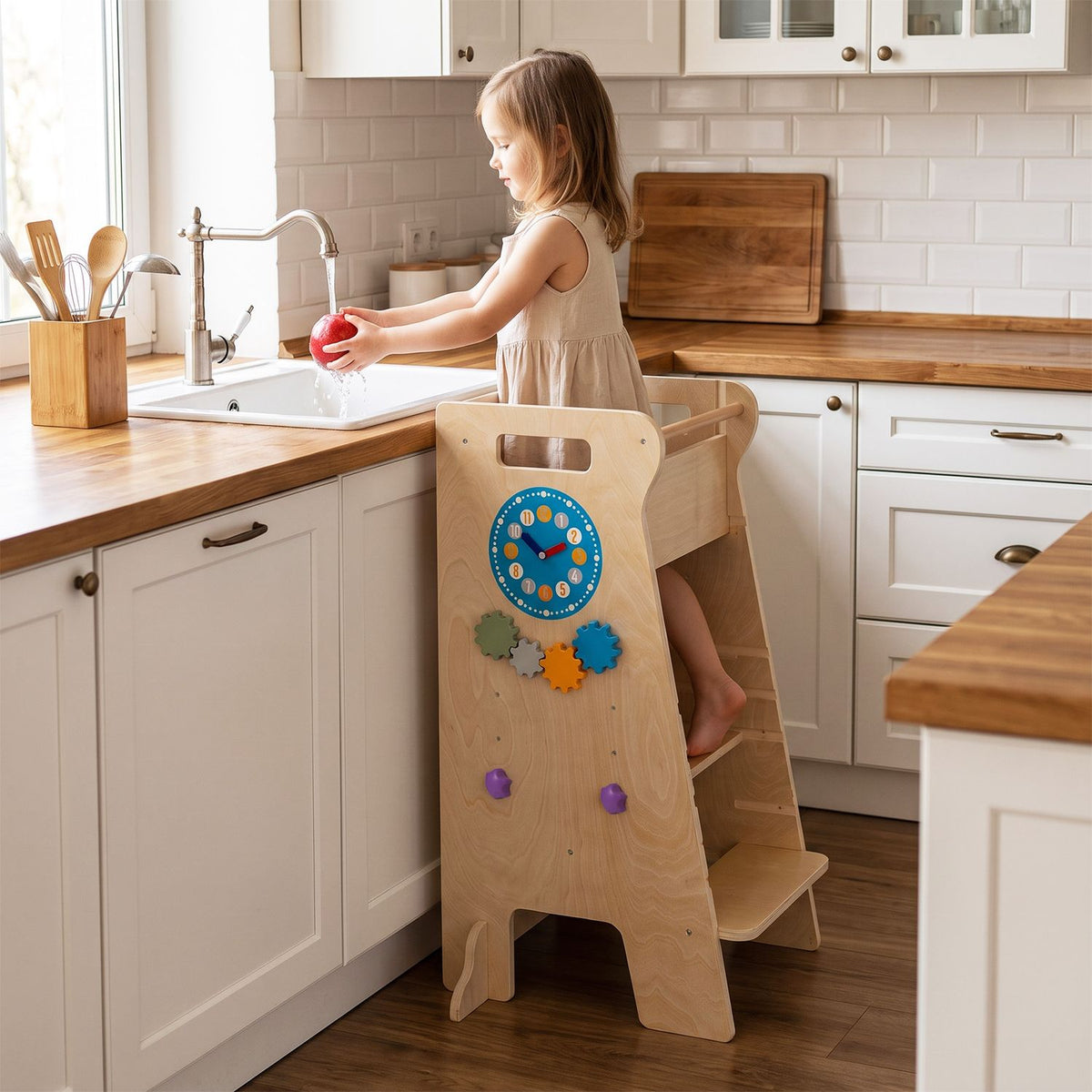 A child stands in a wooden tower at the kitchen sink, with colorful activity pieces on its side panel.