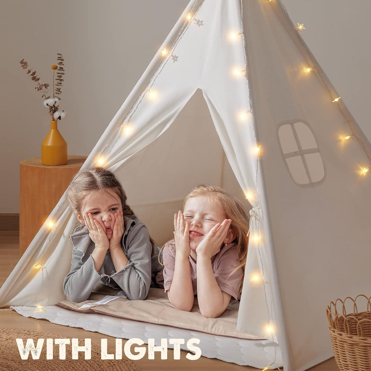 Two young girls lying inside a white canvas teepee decorated with star string lights