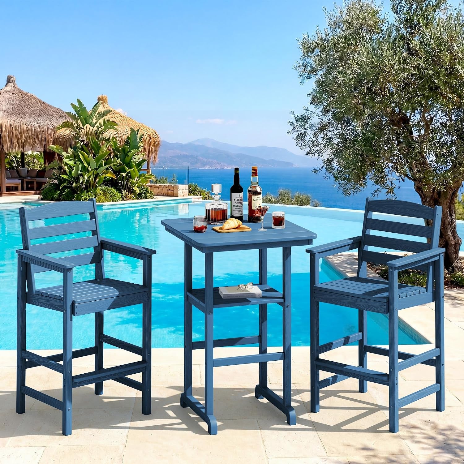 Blue bar table and two blue armchairs positioned poolside with coastal view and bottles on the table