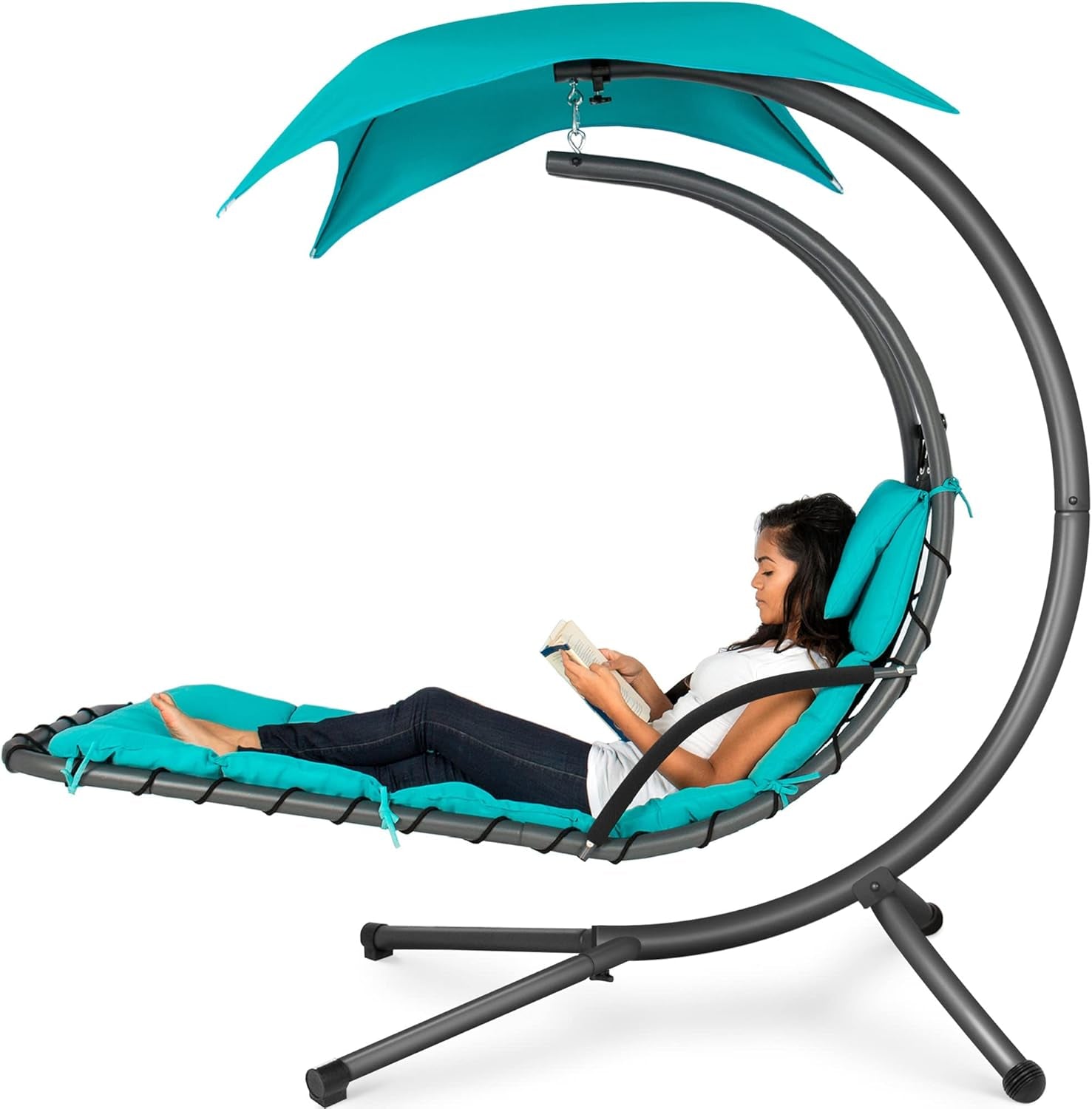 Side view of teal hanging curved chaise lounge with canopy and a woman reclining and reading.