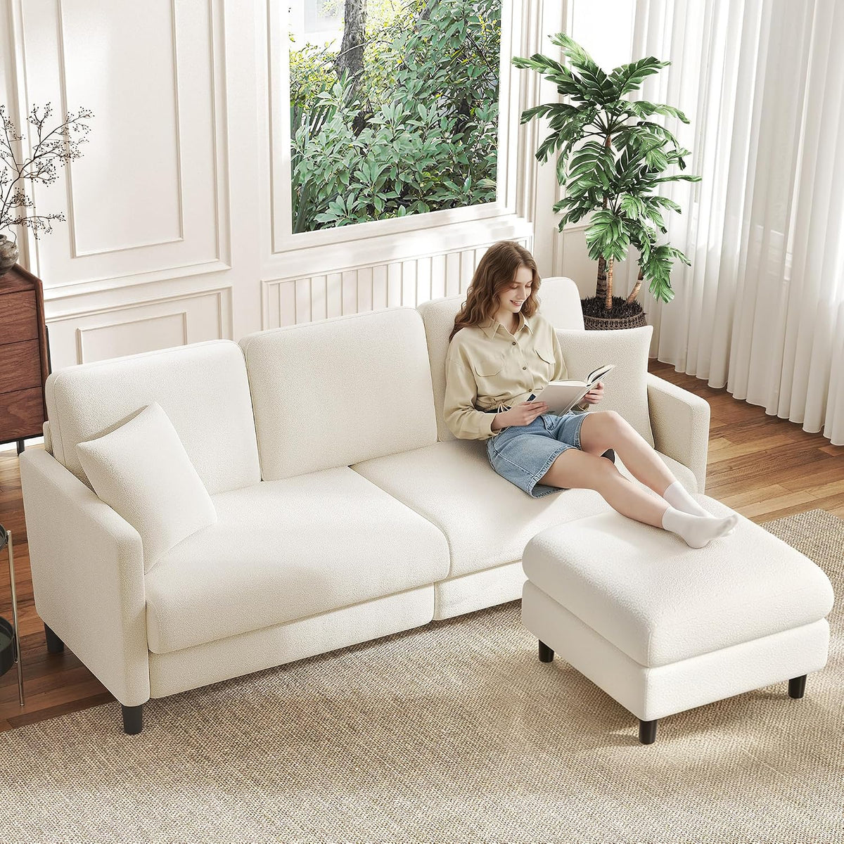 White sofa and ottoman in a bright room with a woman lounging and reading a book