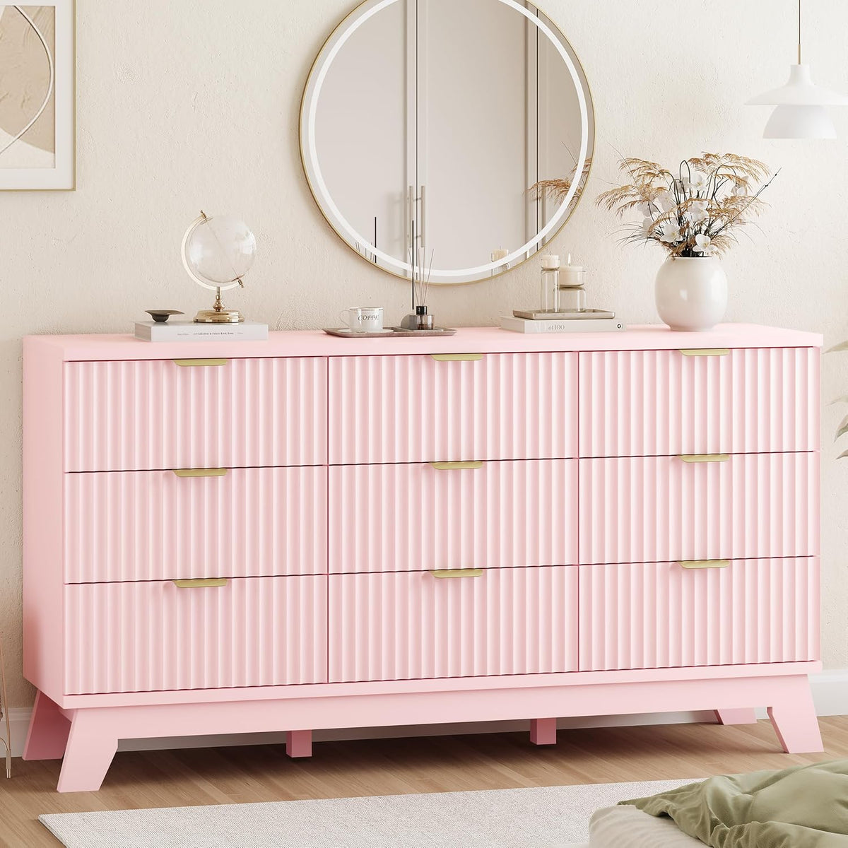 Wide nine-drawer pink dresser with fluted fronts, gold handles and round mirror above.