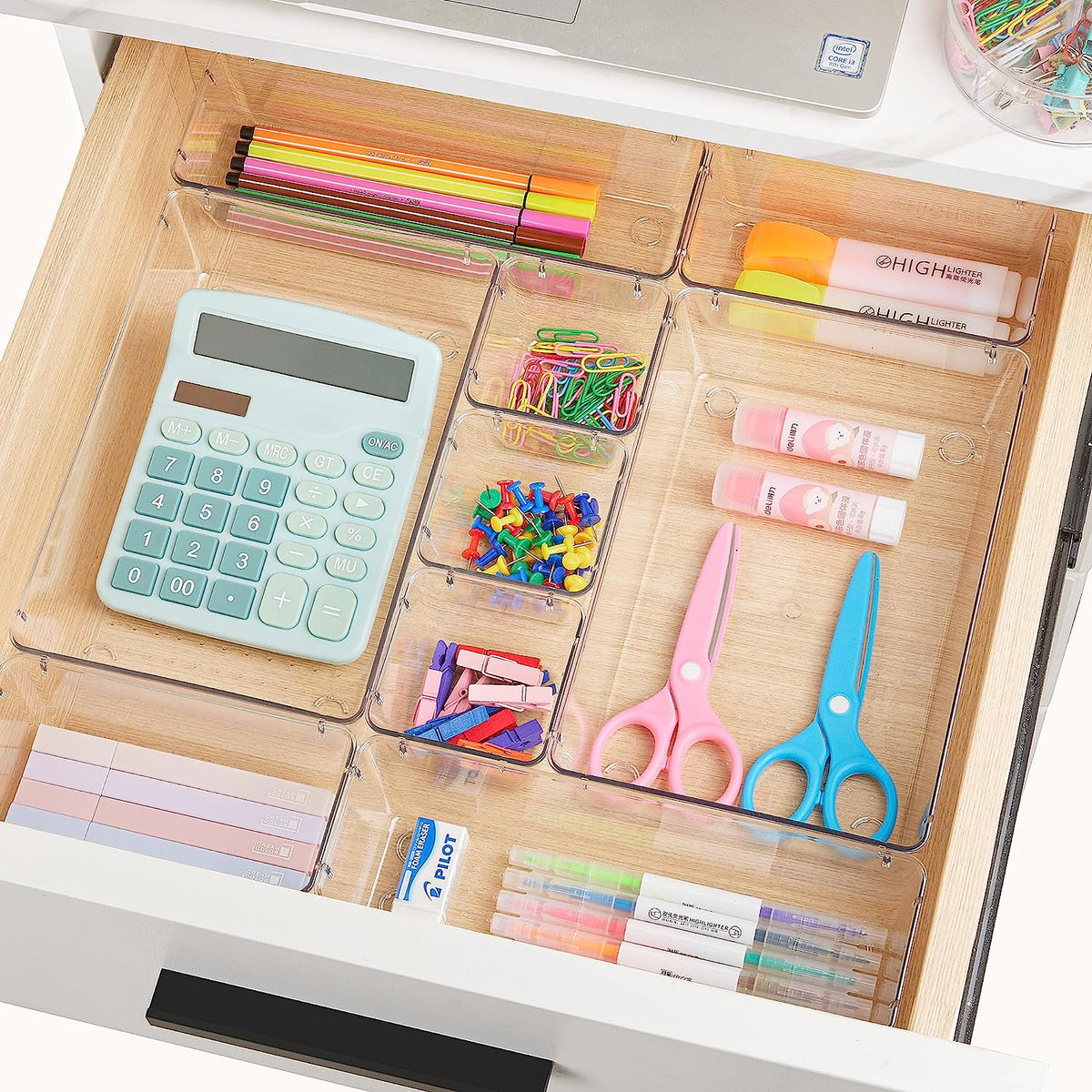 Clear trays in a desk drawer organizing pens, highlighters, calculator and small office supplies