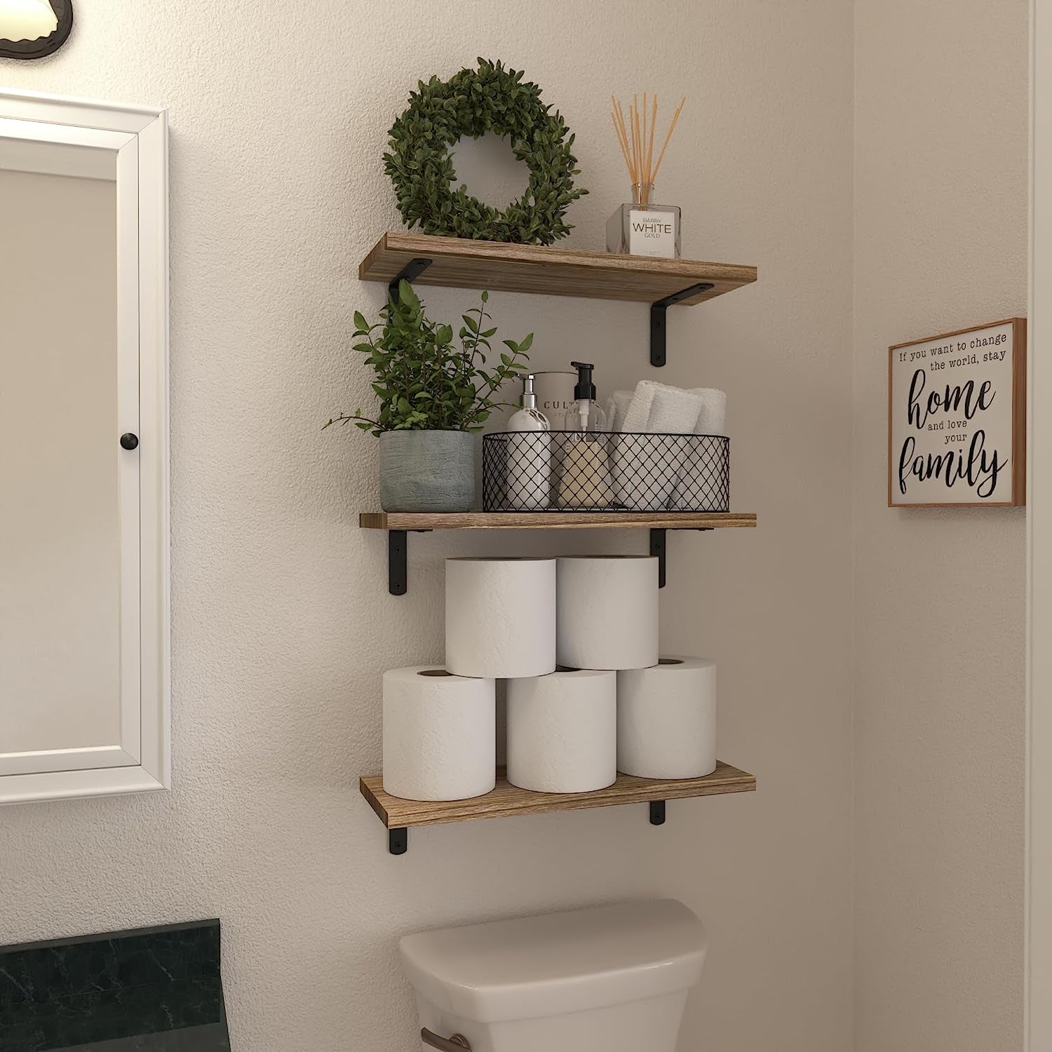 Three rustic brown floating shelves above a toilet holding decorative items and stacked toilet paper rolls