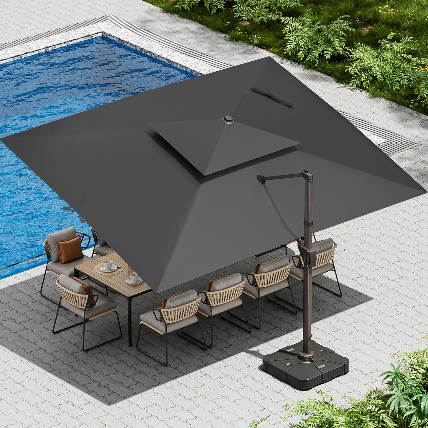 Overhead view of a dark gray cantilever umbrella shading an outdoor dining set next to a pool