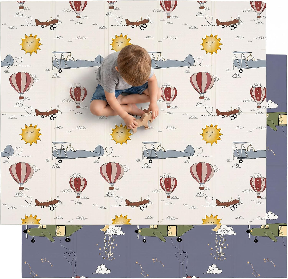 Overhead view of a child playing on a cream mat printed with suns, hot air balloons and biplanes; a navy