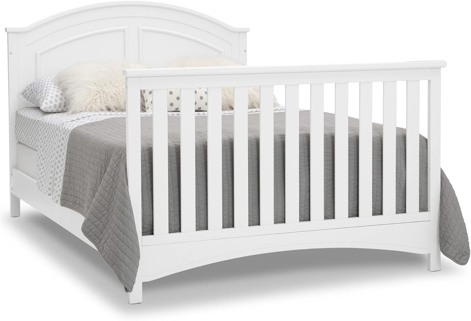Angled side view of the white crib showing vertical slats on the footboard and curved lower apron.