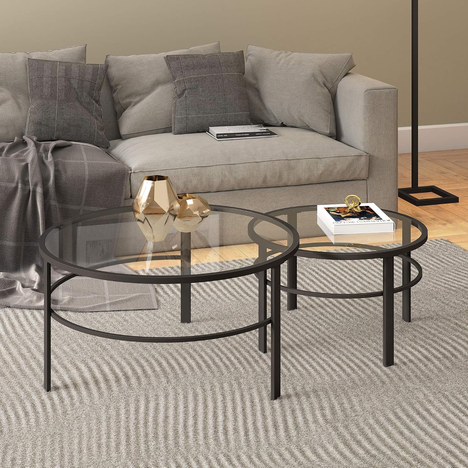 Round tempered glass nesting coffee tables in blackened bronze in a living room setting beside a gray sofa