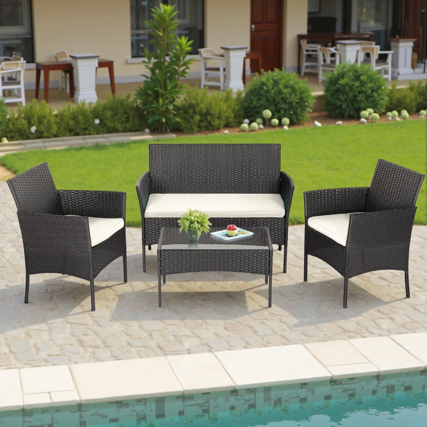 Four-piece dark rattan patio set with two armchairs, a two-seat bench and glass-top coffee table beside a pool.