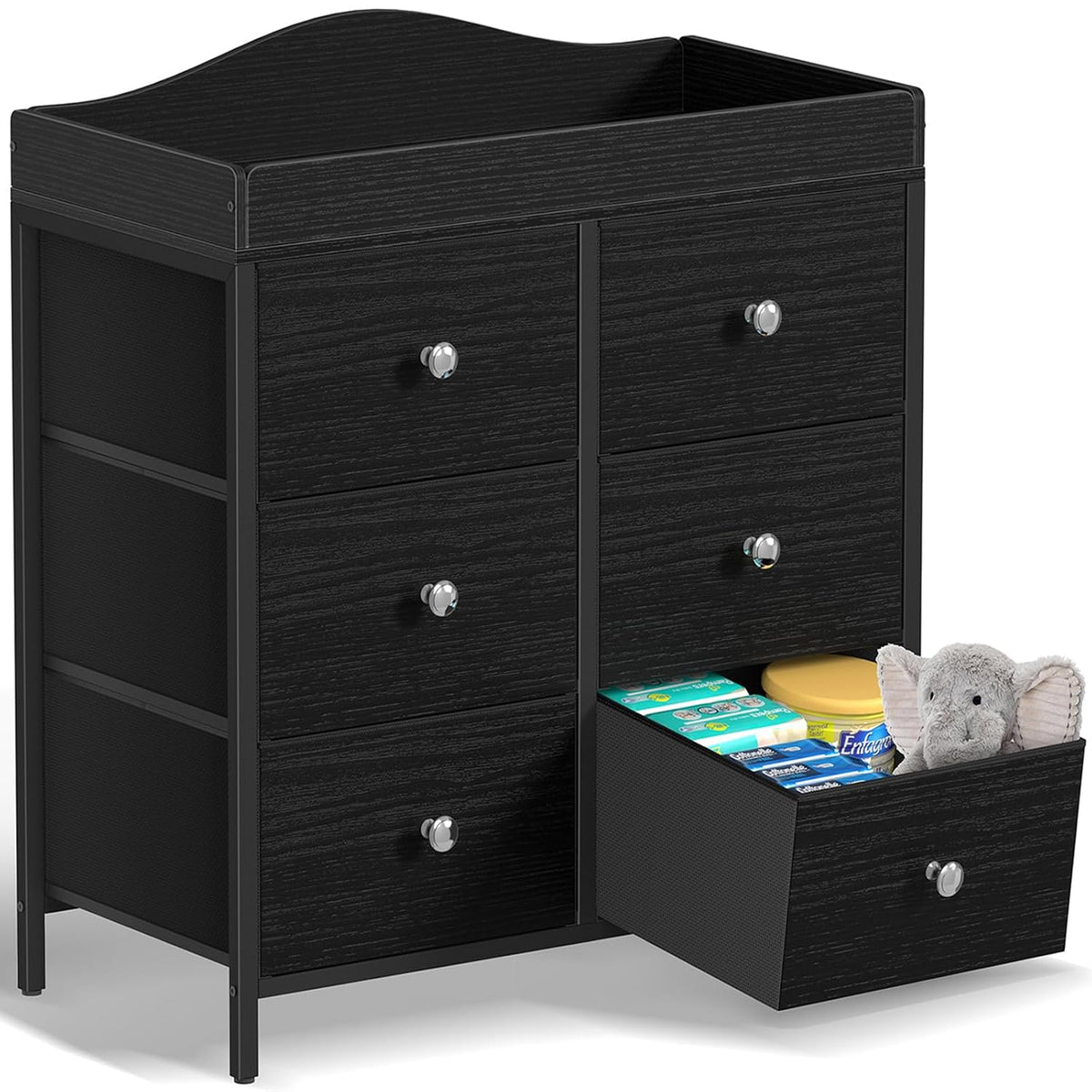 Black six-drawer changing dresser with one lower drawer open showing baby supplies and a stuffed elephant.