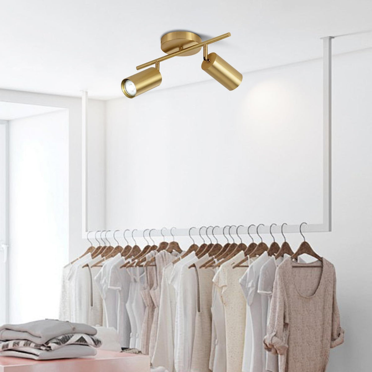 Gold finish 2-light ceiling track fixture shown above a clothing rack in a retail-style room setting