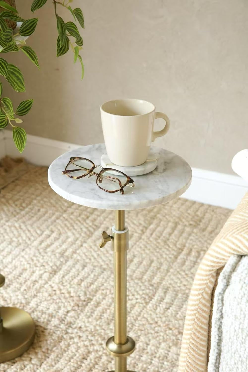 Small round white marble side table with antique brass pedestal next to a chair, mug and glasses on top.
