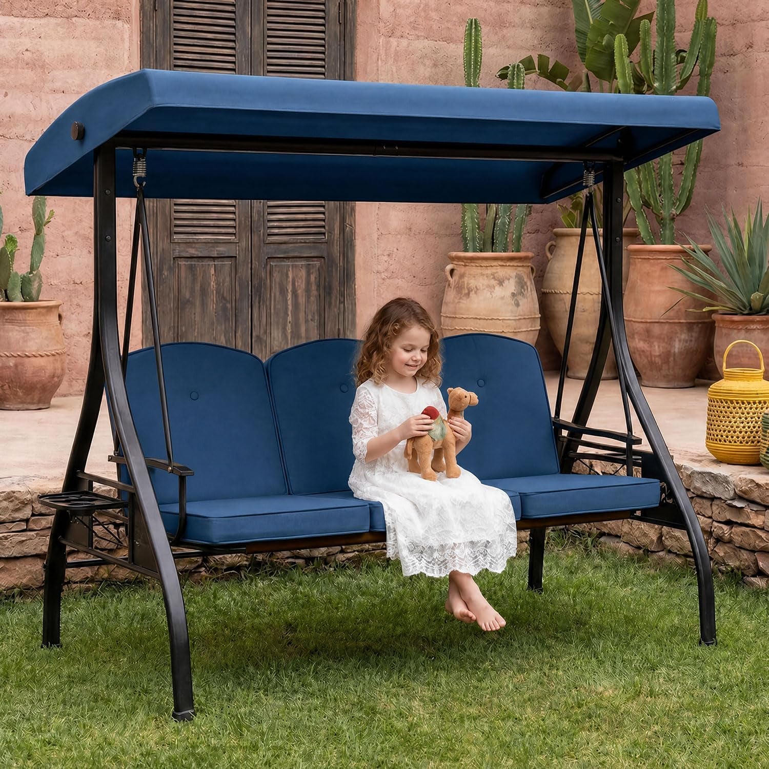 Blue-cushioned three-seat porch swing with canopy; a young girl sits holding a stuffed toy.