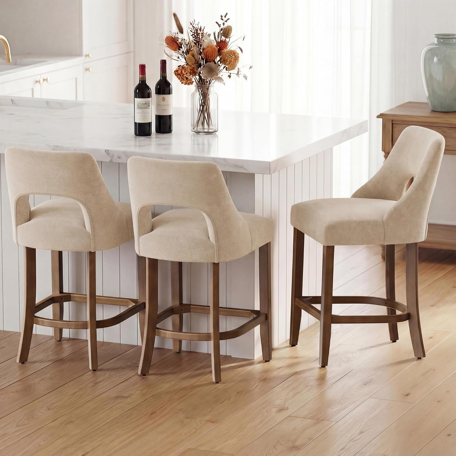Low-angle view of three beige counter stools showing wood legs, footrests and floor pads under island