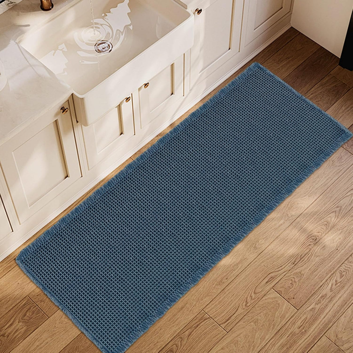 Long blue waffle bath runner placed in front of a white sink on wood flooring, showing texture.