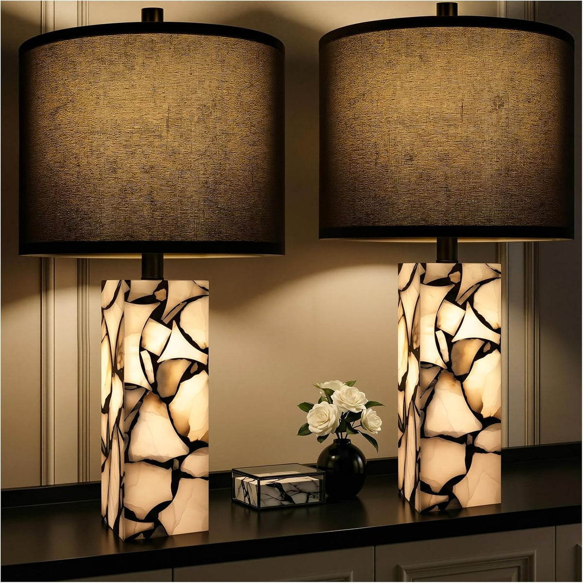 Pair of illuminated rectangular alabaster bases with dark drum shades on a console and small black vase