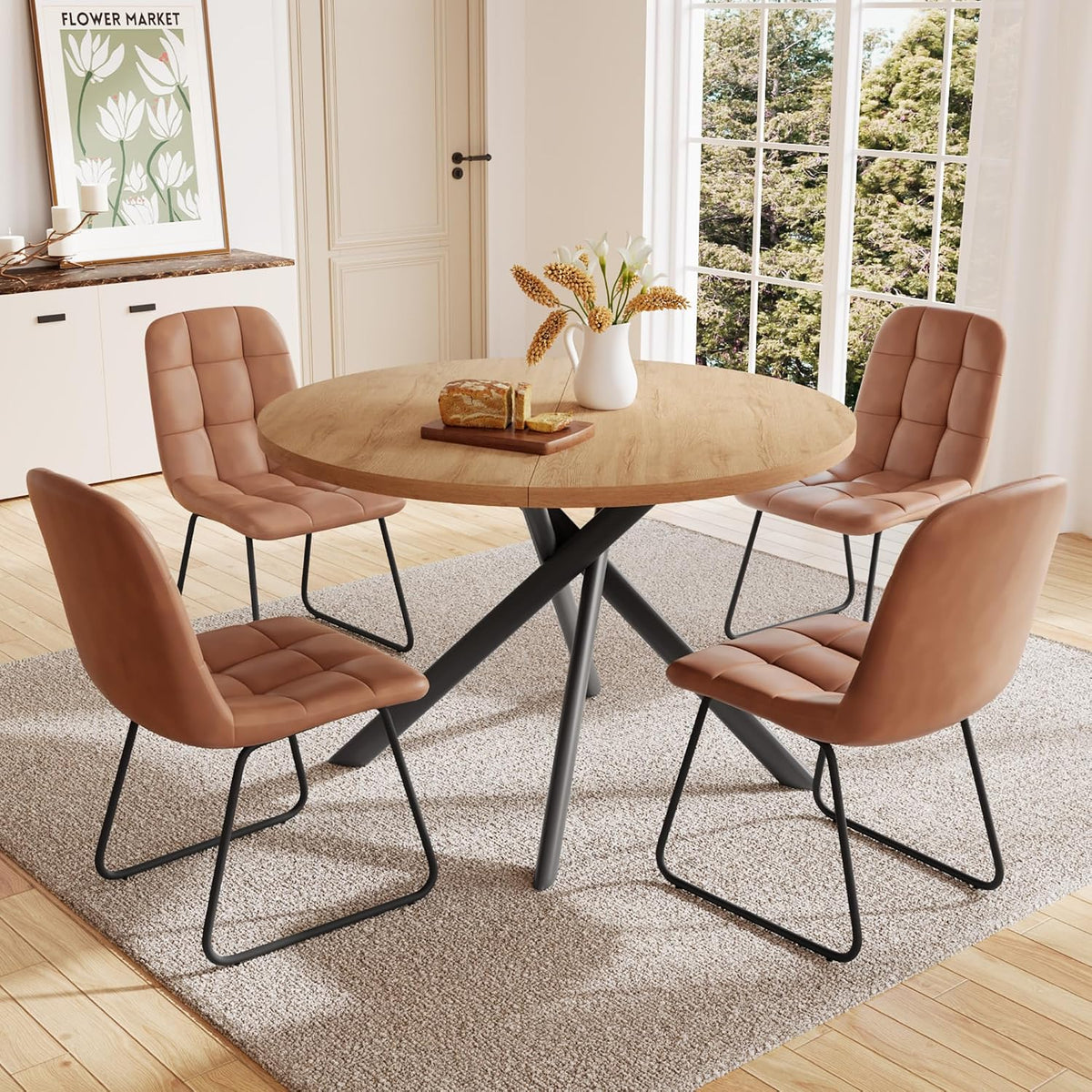 Round light-wood dining table with four tan upholstered U-shaped chairs in a bright room.