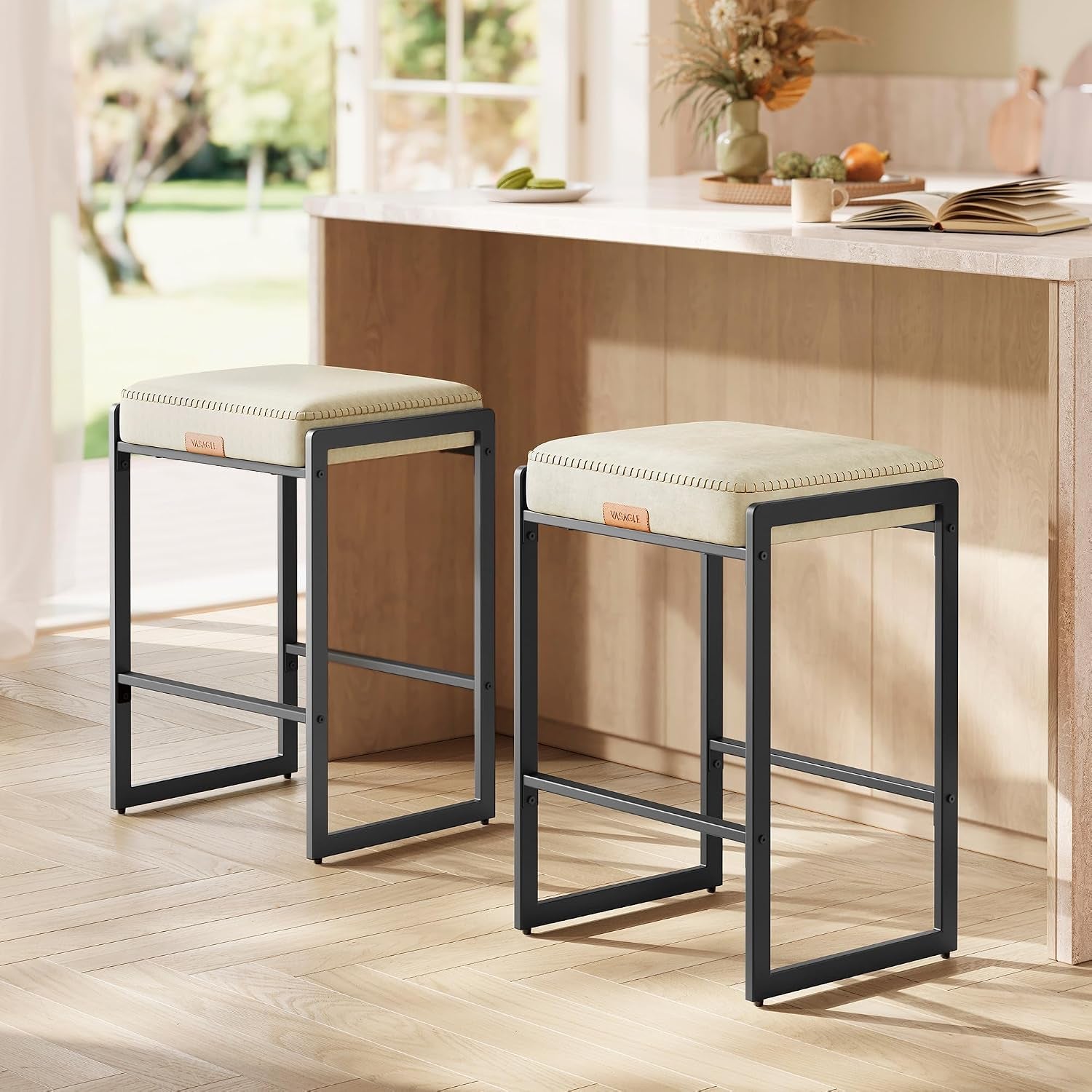 Pair of light beige cushioned counter stools with black rectangular metal frames beside a light wood island.