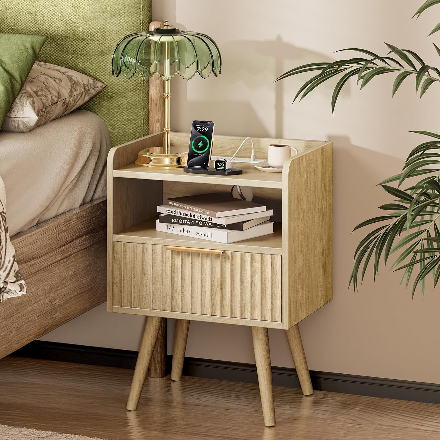 Walnut nightstand with fluted drawer and open shelf next to bed, lamp, charging phone, books and mug visible