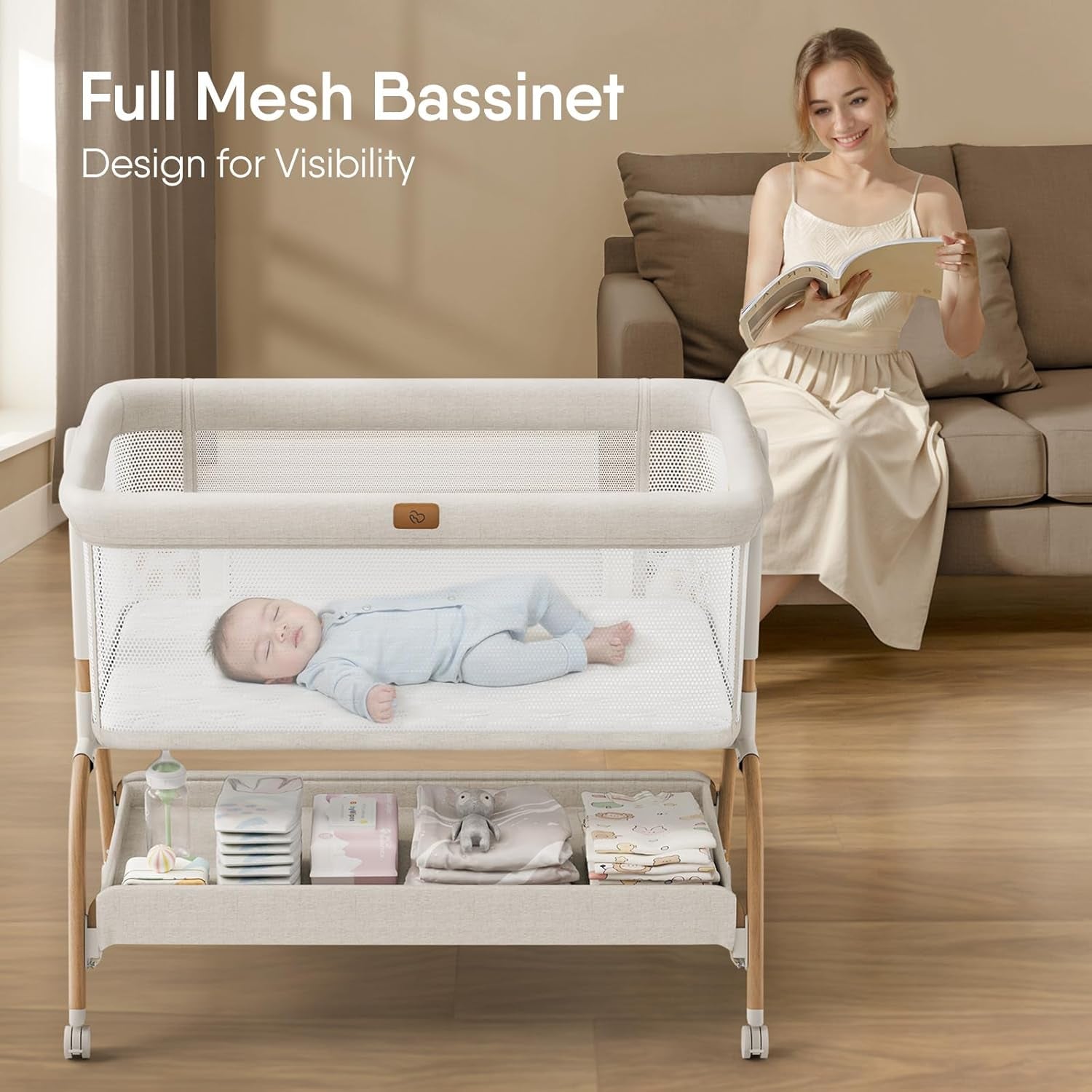 Front-facing shot showing the full mesh bassinet in beige with a baby sleeping and a woman reading on a sofa behind it.