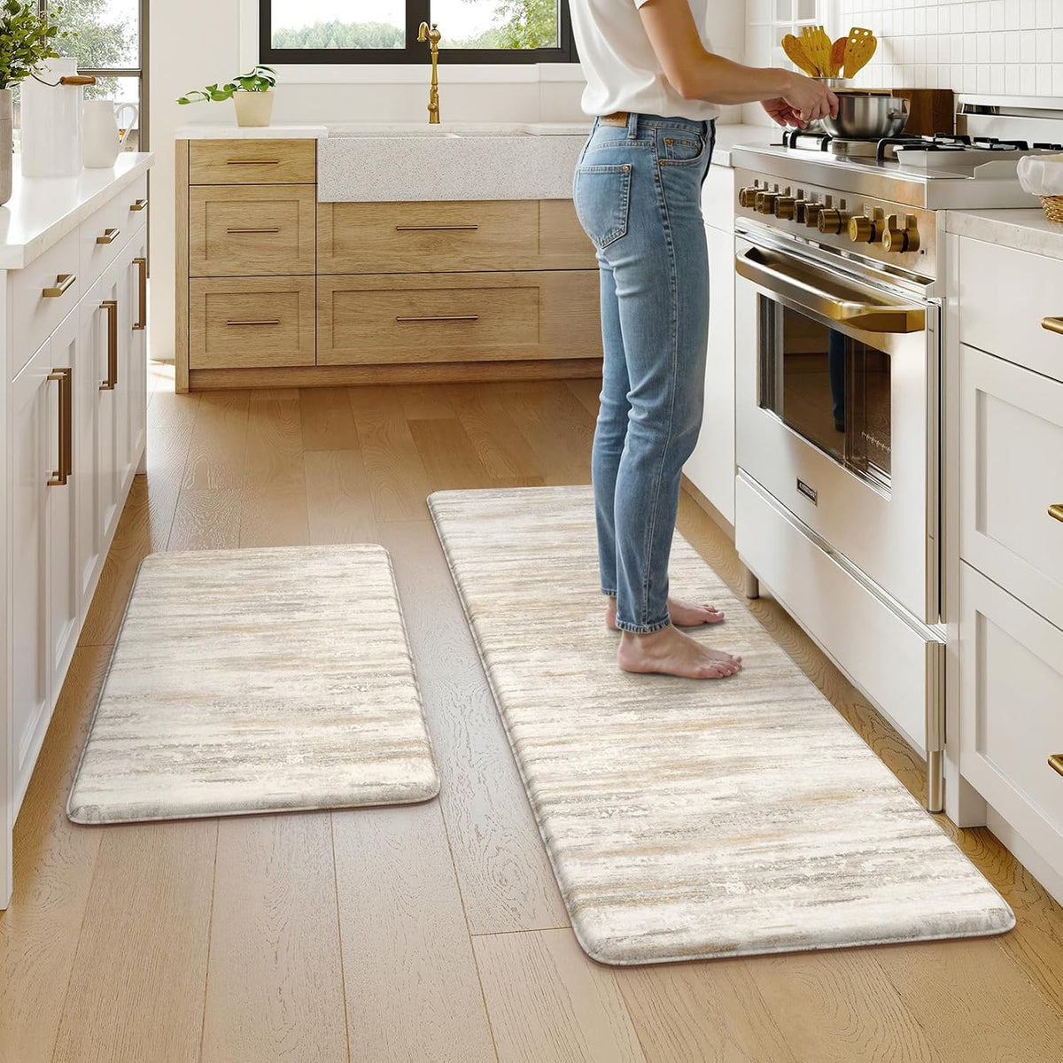 Two beige matching kitchen mats laid along a light-wood floor with a person standing at the stove